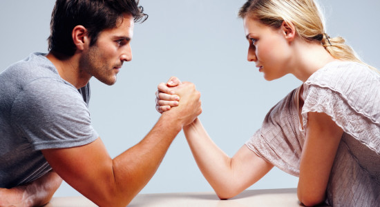 Young couple arm wrestling against grey background